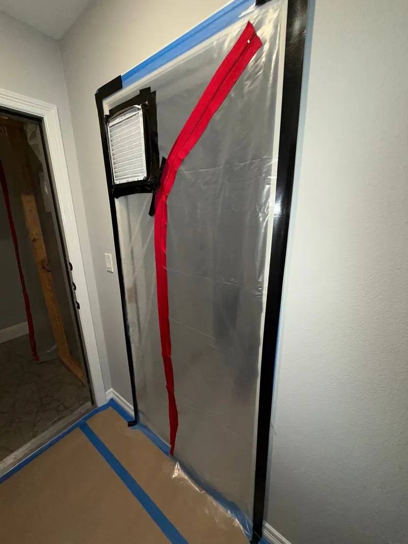 Plastic containment wall with a zipper door and an air filter panel sealing off a room