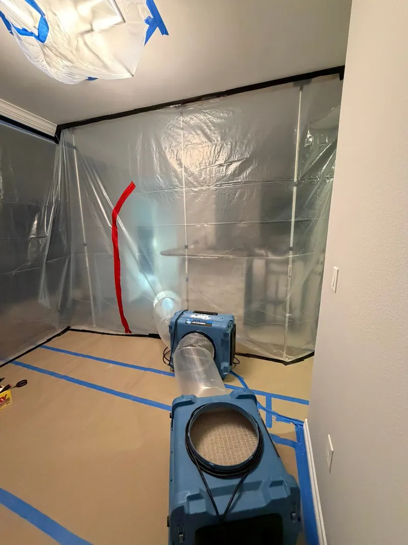 Room sealed with plastic sheeting and tape for mold remediation, with a HEPA air scrubber duct on the floor