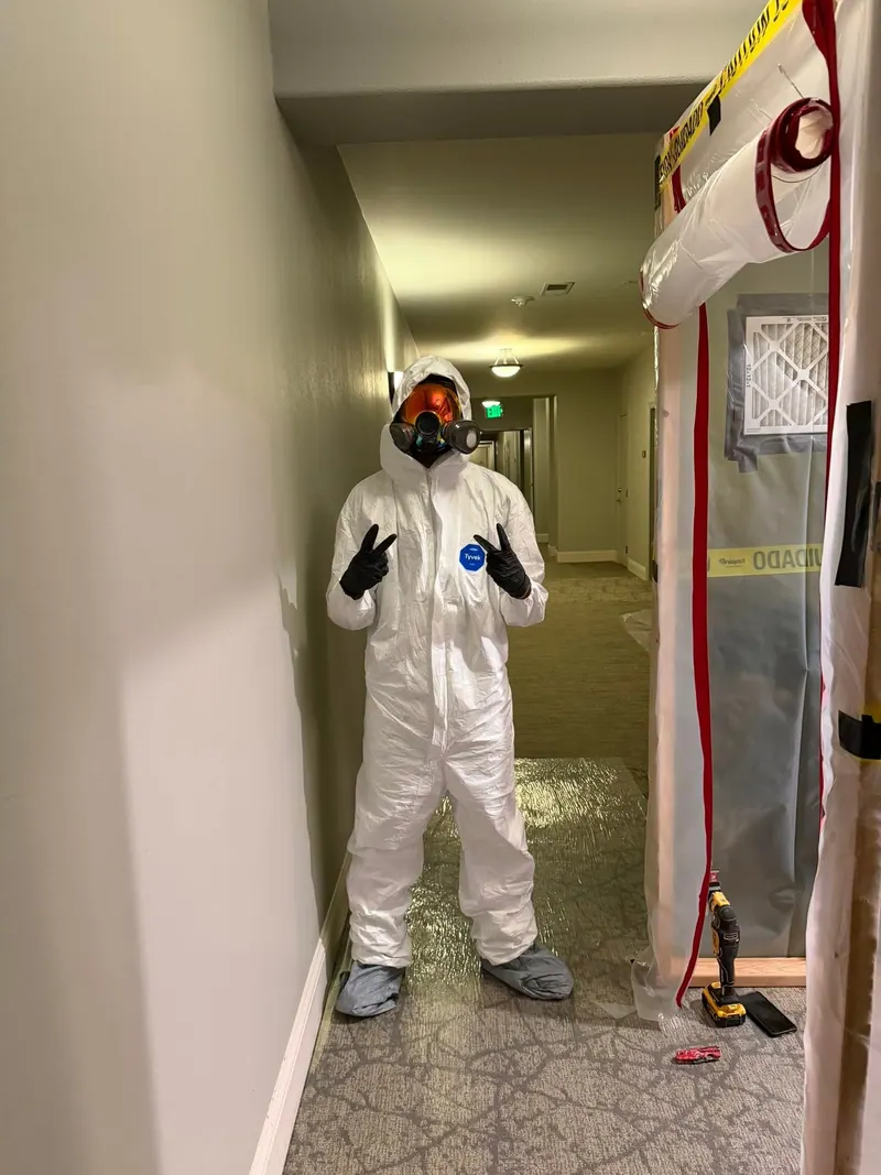 Remediation technician in a full protective suit and respirator standing beside a sealed containment door