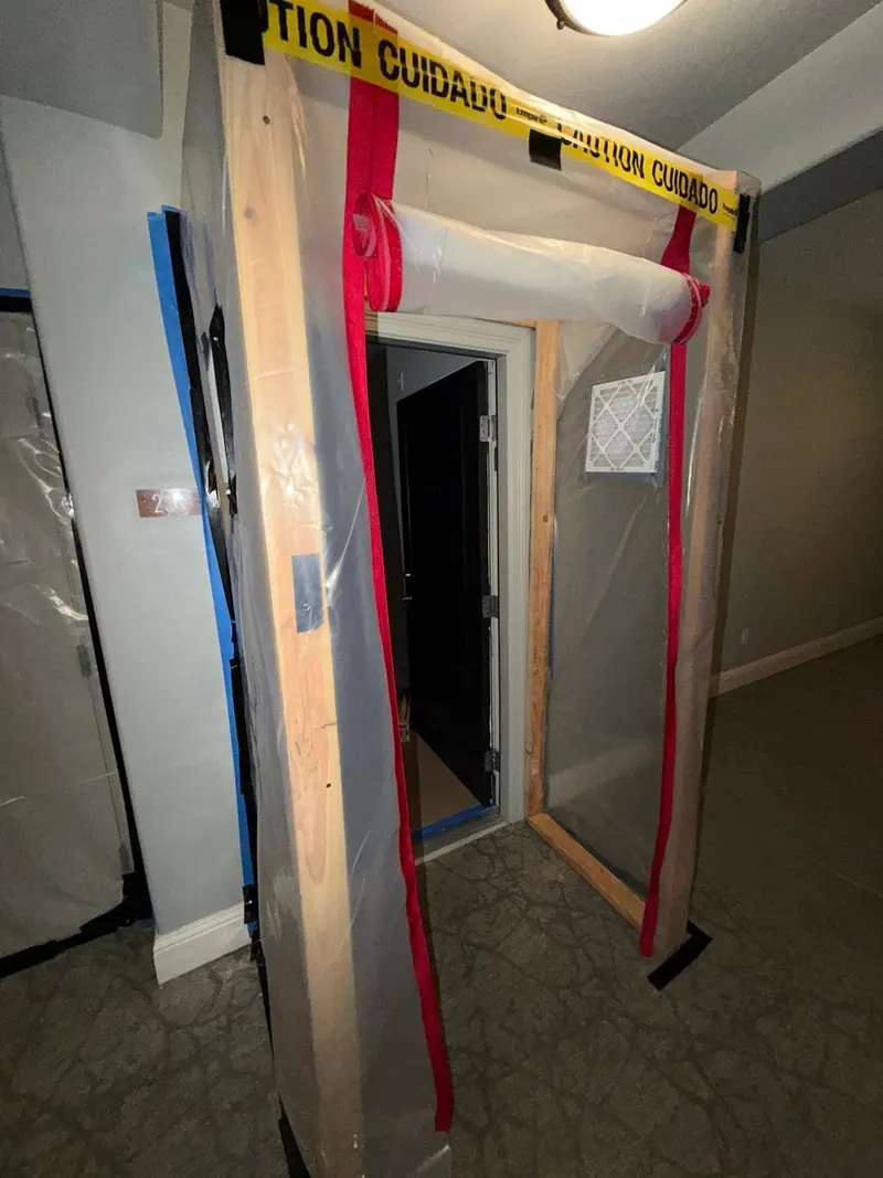 Hallway entrance sealed with plastic sheeting, a framed zipper door and caution tape